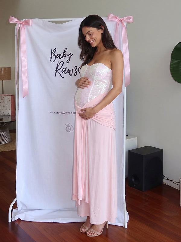 Roze babyshower zwangerschaps jurk met glanzende pailletten, geplooide details en knoopdetail.