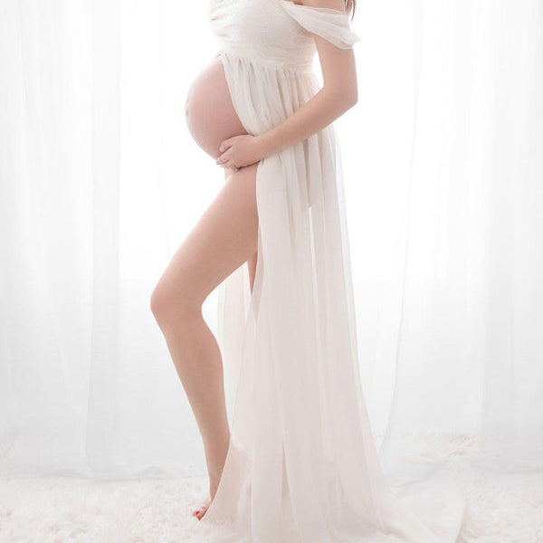 Witte zwangerschaps maxi jurk met kanten bandeau hals, chiffon stof en elegante zijsplit voor fotoshoot.