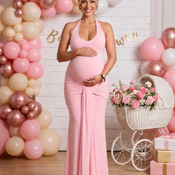 Roze zwangerschaps maxi jurk met halterhals, gedrapeerde details en open rug, ideaal voor babyshower.
