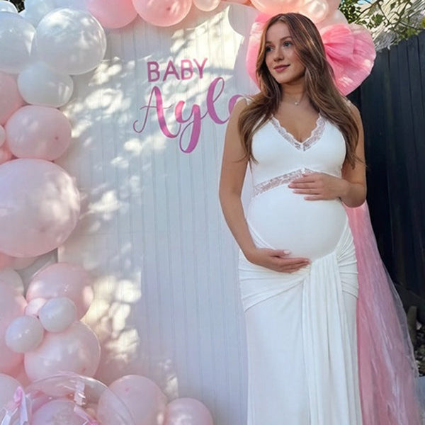 Witte zwangerschaps maxi jurk met kanten patchwork, strikdetail en gedrapeerde pasvorm, ideaal voor een babyshower.