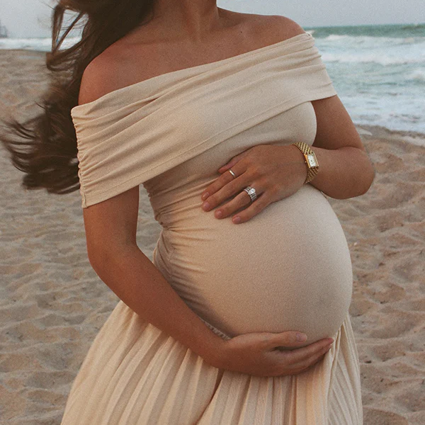Abrikooskleurige zwangerschaps maxi jurk met off-shoulder en bodycon pasvorm, ideaal voor strand fotoshoots.