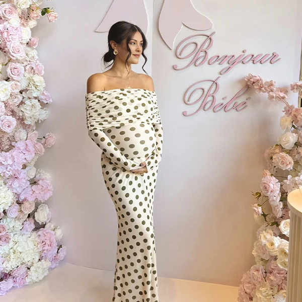 Witte zwangerschaps maxi jurk met olijfgroene stippen en off-shoulder, ideaal voor een babyshower.