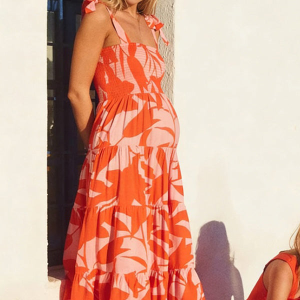Oranje zwangerschaps maxi jurk met bloemenprint, ruches en spaghettibandjes, ideaal voor vakantie.
