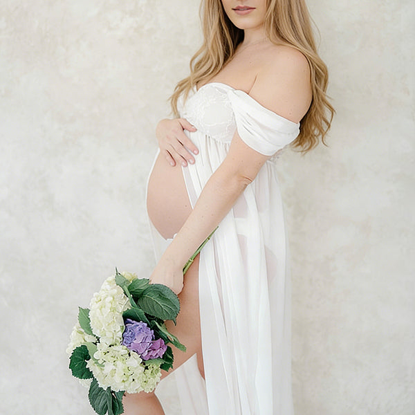 Witte zwangerschaps maxi fotojurk met bandeau hals, opengewerkt design en zijsplit voor fotoshoot.
